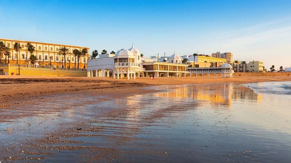 Capture the serenity of Playa de la Caleta with its golden sands and crystal-clear turquoise waters, nestled between rugged cliffs and lush greenery