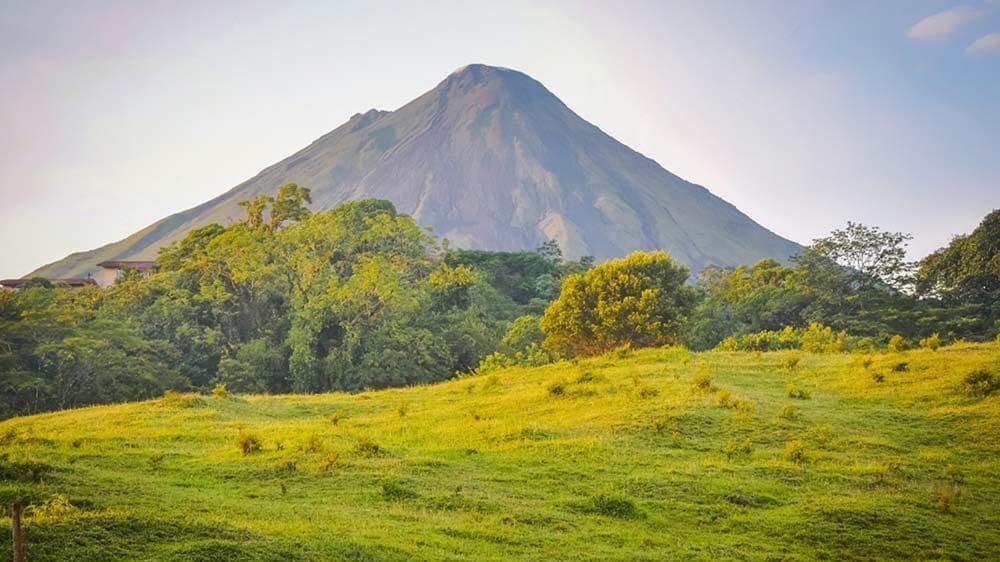 Captivating view of the majestic Volcán Arenal towering above lush green forests, with billowing white clouds engulfing its summit
